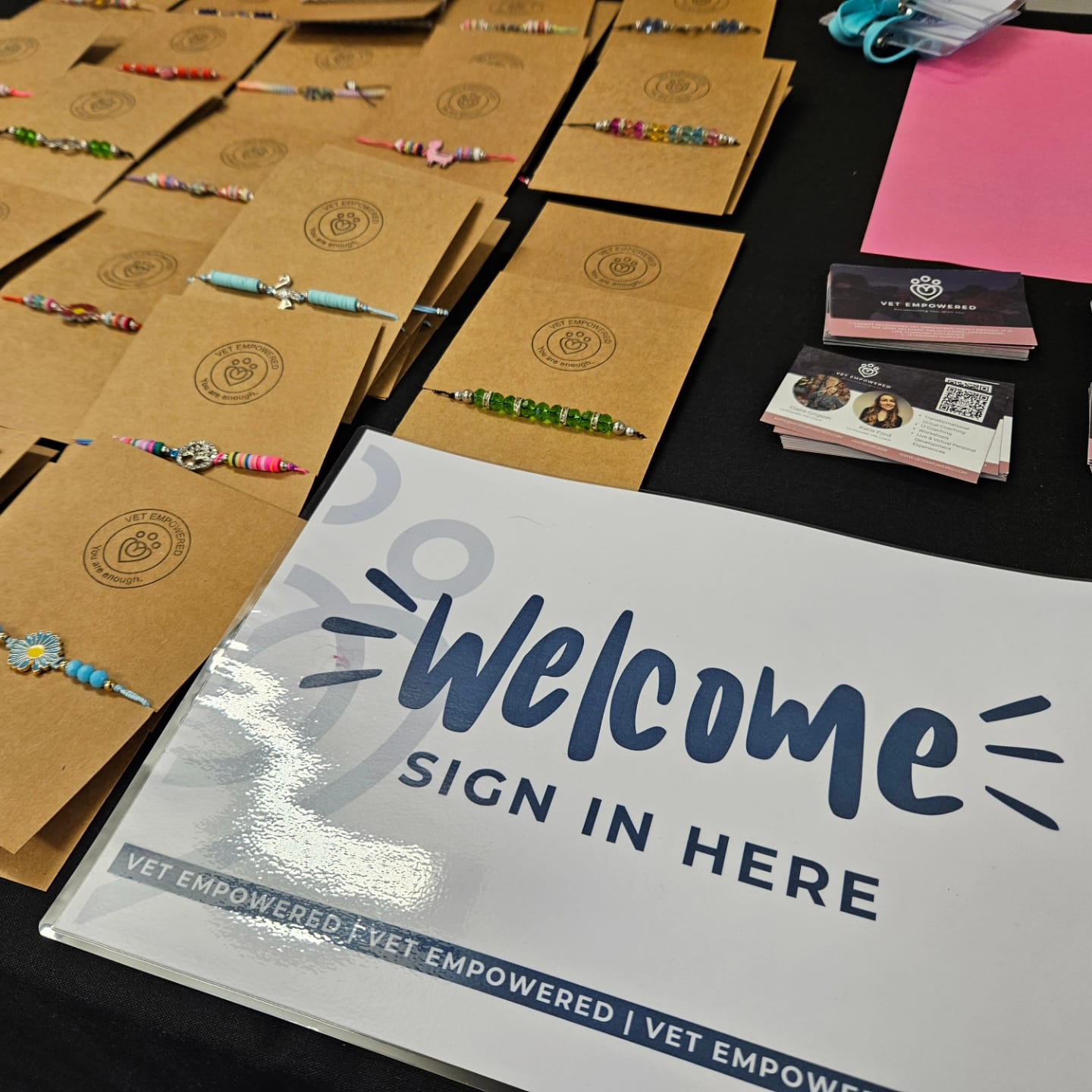 A Vet Empowered welcome table with a sign reading Welcome Sign In Here, alongside handmade bracelets and business cards.